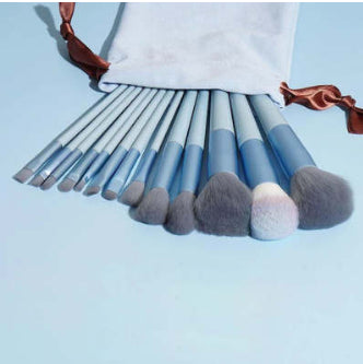 Set of makeup brushes with gray bristles in a white pouch on a light blue background