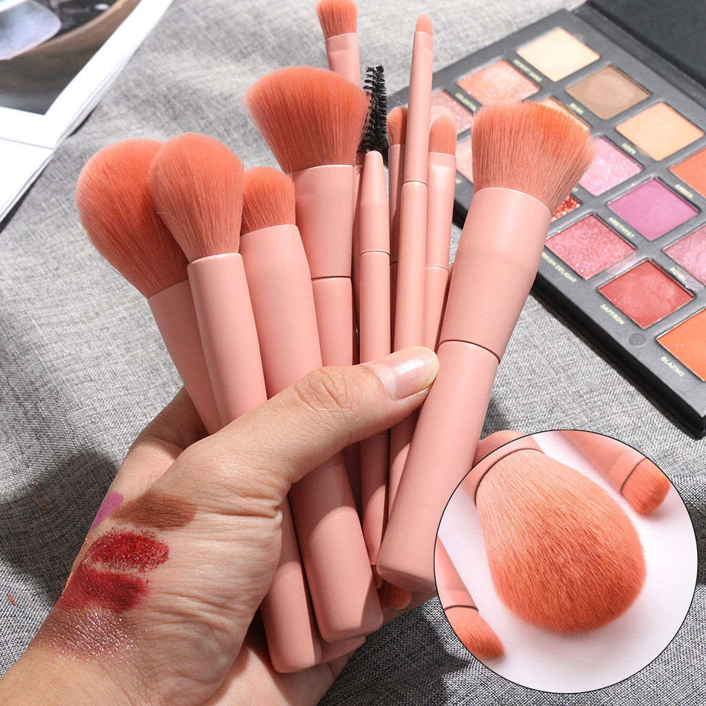 Set of makeup brushes with pink handles held by a hand, with an inset showing brush detail.