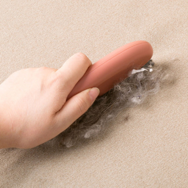 Hand using a red tool to remove pet hair from a beige carpet