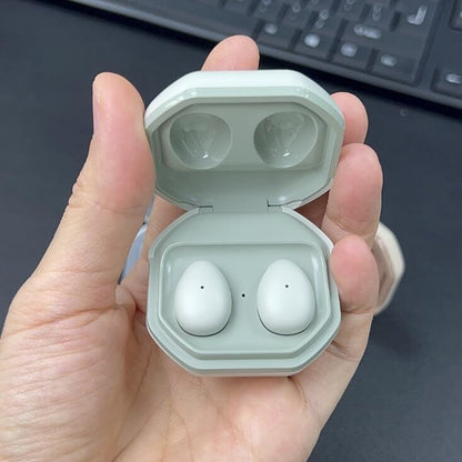 Hand holding a light gray case with wireless earbuds against a blurred keyboard background