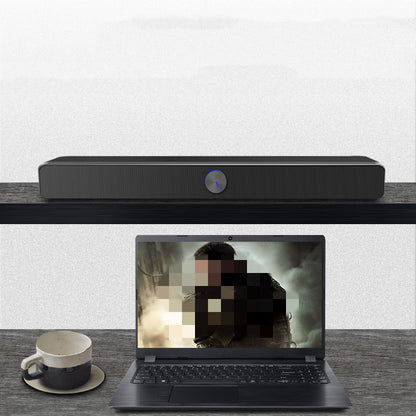 Black soundbar on a table with a laptop displaying a blurred image below it.
