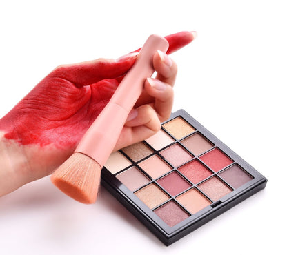 Makeup palette with a brush and hand applying red makeup on a white background