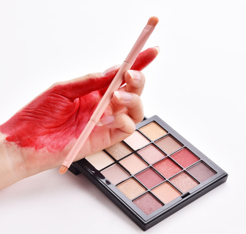 Makeup palette with a brush and hand holding red lipstick on a white background