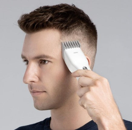 Man using a hair trimmer on his head against a gray background