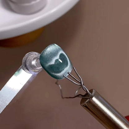 Close-up of a greenish-blue object held by tweezers on a brown background