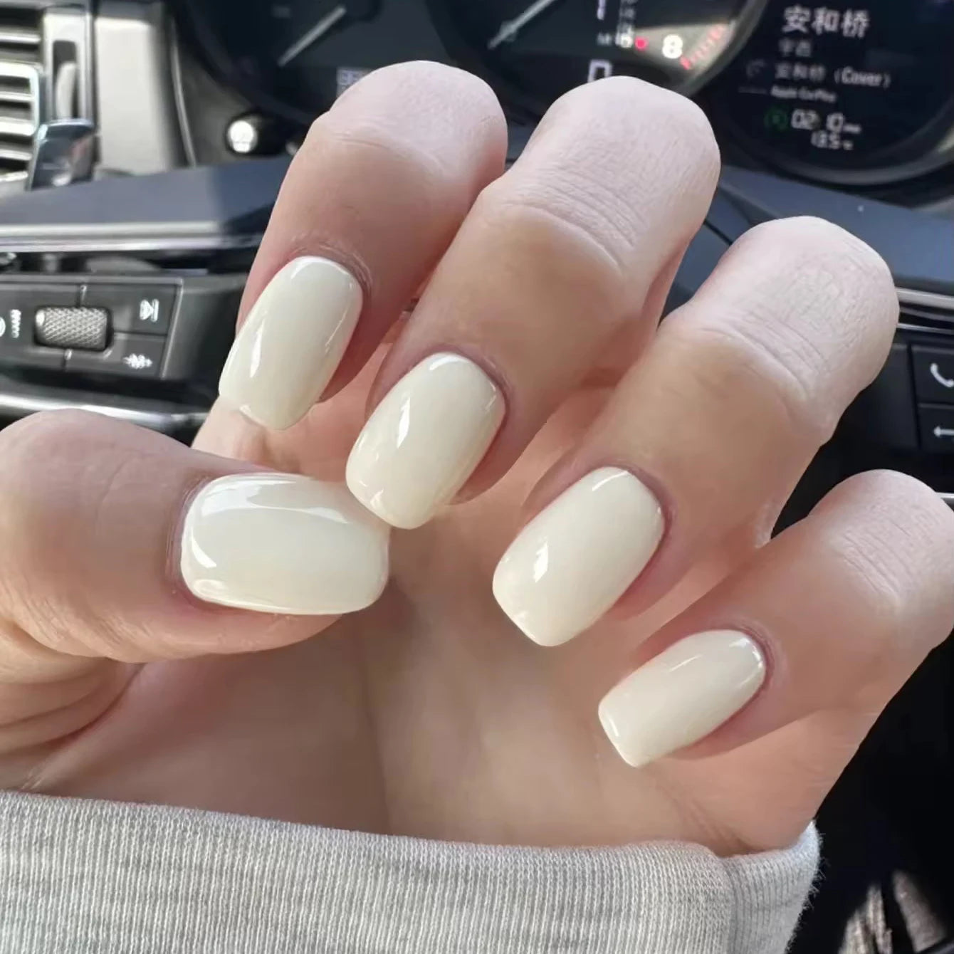 Hand with white nail polish in a car interior