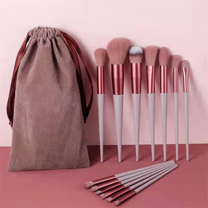 Set of makeup brushes with a brown drawstring bag on a pink background