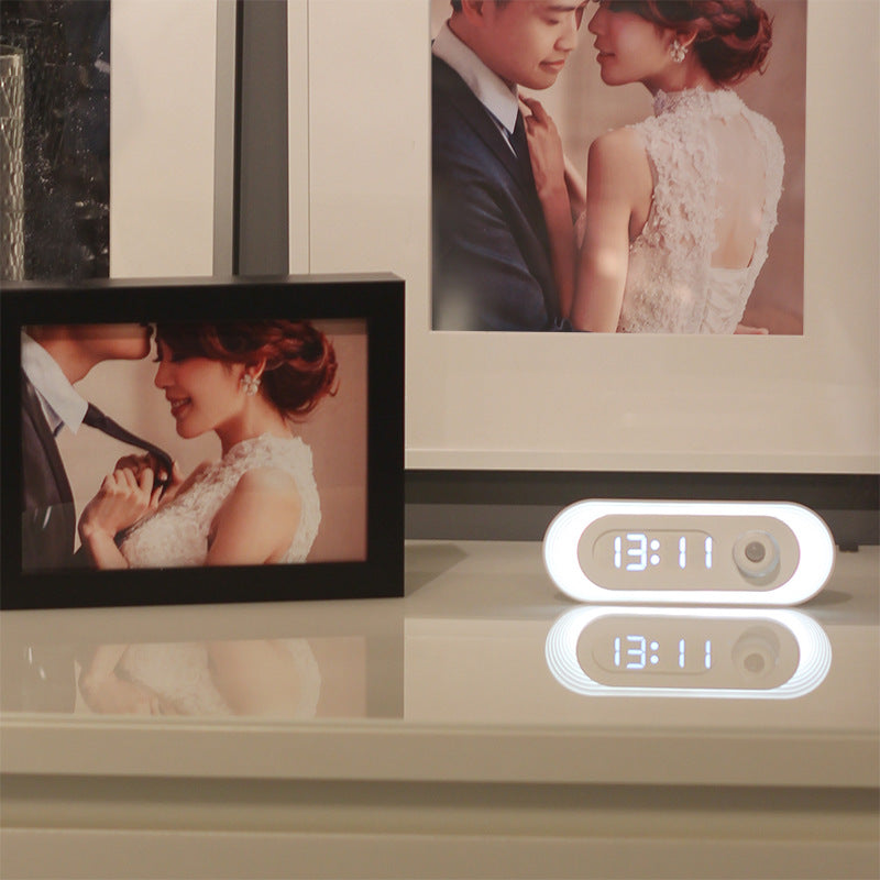 Digital clock on a surface with two framed pictures of a couple in formal attire.