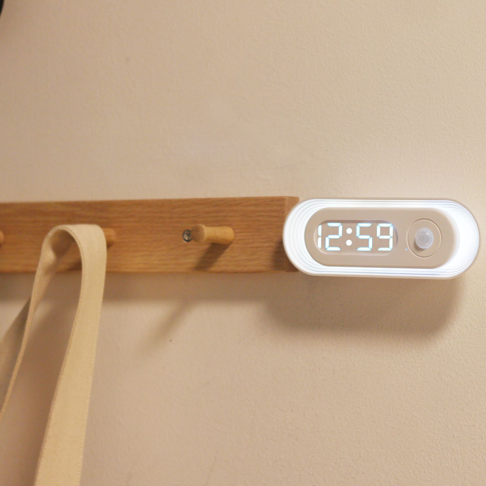 Wooden wall hook with digital clock displaying 12:59 on a beige background