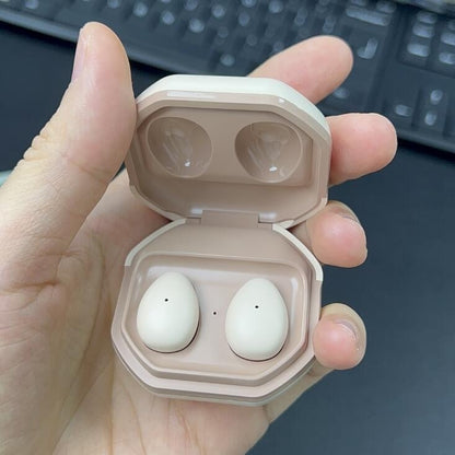 Beige wireless earbuds in an open case held by a hand with a keyboard in the background.